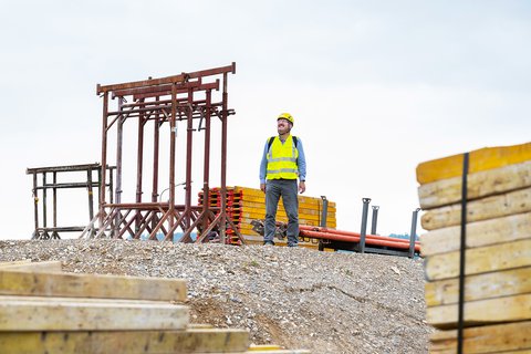 Thomas Varga, Projektleiter Energie 360° mit gelber Sicherheitsweste und Helm auf Erdhügel einer Baustelle