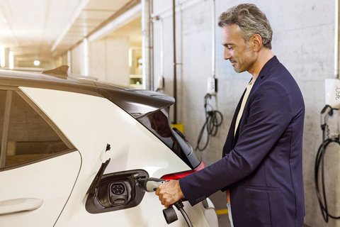 Un homme branche sa voiture électrique à la borne de recharge de sa place de parc.