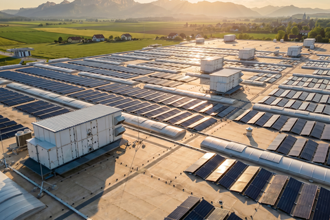 Grossflächige Solaranlage auf dem Flachdach eines Industriegebäudes bei tief stehender Sonne, Batteriespeicher zwischen den Solarmodulen