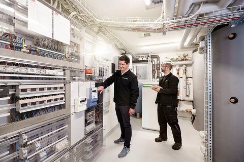 Zwei Männer in einem Raum mit Schaltschränken und Heizungsspeichern
