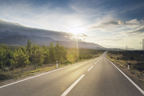 Eine kurvige Landstrasse in den Bergen mit der Sonne im Hintergrund