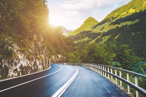 Eine kurvige Landstrasse in den Bergen mit der Sonne im Hintergrund