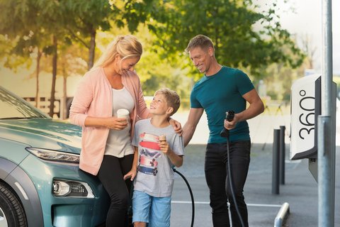 Une famille se tient entre une colonne de recharge d’Energie 360° et un e-véhicule. Le père tient le câble de recharge à la main.