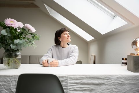 Adepte du minimalisme, Alessia Baumgartner est assise à table dans son appartement avec une tasse de thé et des fleurs, et regarde par la fenêtre de toit