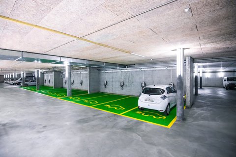 Une voiture électrique blanche se recharge sur une wallbox dans un parking souterrain.