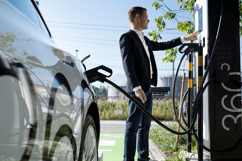 Un homme en costume recharge sa voiture électrique à une station-service électrique d’Energie 360°