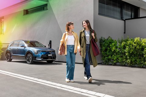 2 weibliche Personen gehen nebeneinander und im Hintergrund ist ein E-Auto sichtbar