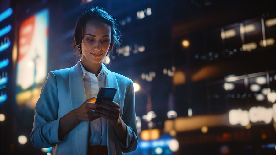 Eine Frau ist abends unterwegs und öffnet dei Swisscharge Lade-App auf ihrem Handy