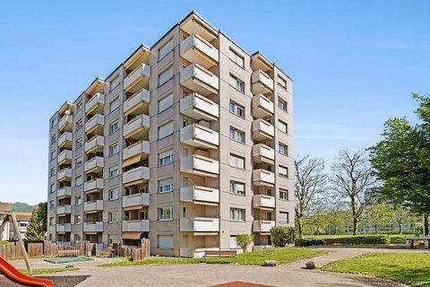 Ein Spielplatz mit roter Rutschbahn und ein Wohnblock im Hintergrund.